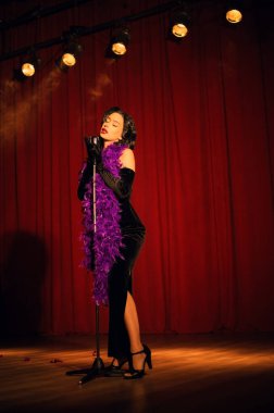 Akşam şovu sırasında kırmızı perdenin önünde mikrofonla sahnede zarif bir sanatçı.