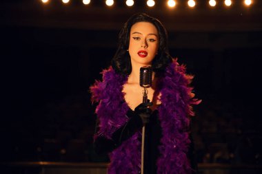 Sahnede klasik tarzda şarkı söyleyen bir kadın. Retro mikrofon ve dramatik ışıklandırmayla.