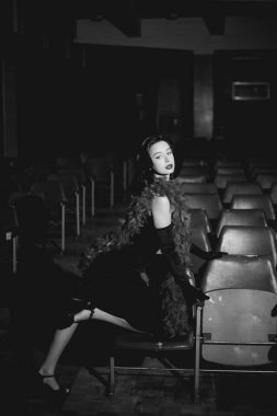 Kaliteli giyinmiş zarif bir kadın geceleri boş bir tiyatroda poz veriyor, göz alıcı bir hava ve sinematik bir atmosfer sergiliyor.