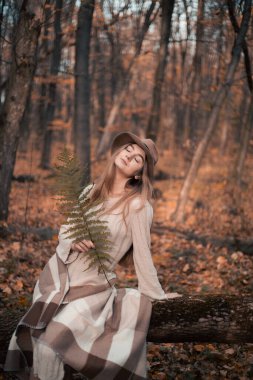 Sonbahar günbatımında eğreltiotu tutan bir kadın düşmüş yapraklarla çevrili.