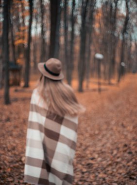 Sonbahar parkında renkli yapraklarla çevrili, rahat bir battaniyenin içinde yürüyüş yapan bir kadın.