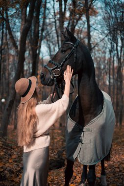 Kadınlar, sonbahar mevsiminde at başında dikilirken şapka ve kazak giyerler.