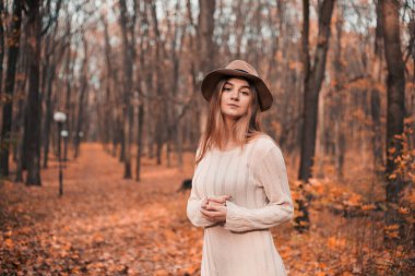 Genç bir kadın, sonbahar ormanında yerde portakal yapraklarıyla huzurlu bir anın tadını çıkarıyor.