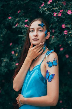 Kelebeklerle dolu yeşil çalıların arasında duran kadın, sıcak bir öğleden sonra sahnesi için bir bahçede poz veriyor.