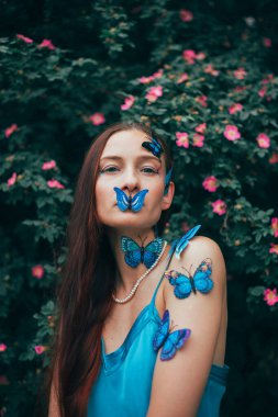 Cildi ve yüzü kelebeklerle kaplı bir kadın gündüzleri çiçeklerin arasında duruyor.