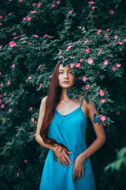 Kelebeklerle dolu yeşil çalıların arasında duran kadın, sıcak bir öğleden sonra sahnesi için bir bahçede poz veriyor.