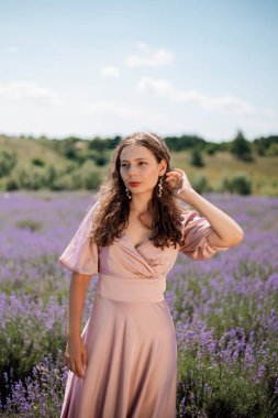 Güneşli bir günde kadın lavanta tarlasında duruyor elleri saçlarında ve nazik bir gülümsemeyle