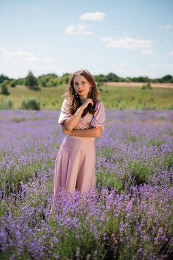 Güneşli bir günde kadın lavanta tarlasında duruyor elleri saçlarında ve nazik bir gülümsemeyle