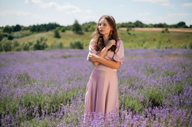 Güneşli bir günde kadın lavanta tarlasında duruyor elleri saçlarında ve nazik bir gülümsemeyle