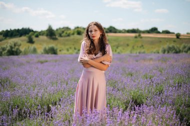 Güneşli bir günde kadın lavanta tarlasında duruyor elleri saçlarında ve nazik bir gülümsemeyle