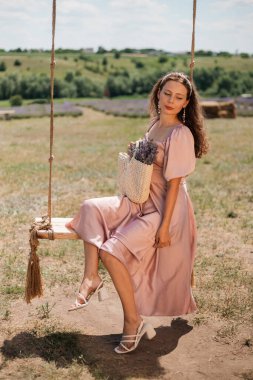 Genç bir kadın güneşli bir günde elinde çiçeklerle salıncakta sallanıyor.