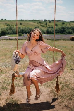 Genç bir kadın güneşli bir günde elinde çiçeklerle salıncakta sallanıyor.