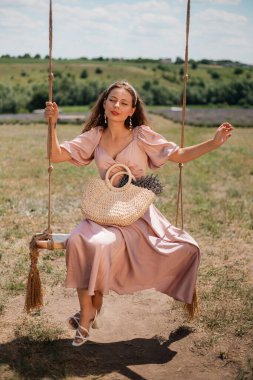 Genç bir kadın güneşli bir günde elinde çiçeklerle salıncakta sallanıyor.