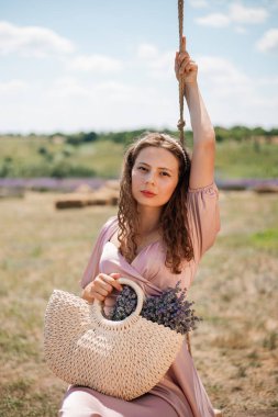 Genç bir kadın güneşli bir günde elinde çiçeklerle salıncakta sallanıyor.