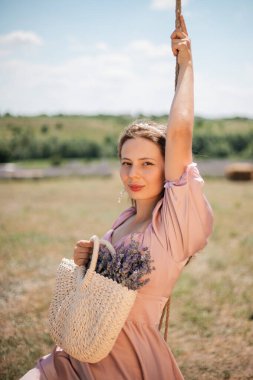 Genç bir kadın güneşli bir günde elinde çiçeklerle salıncakta sallanıyor.