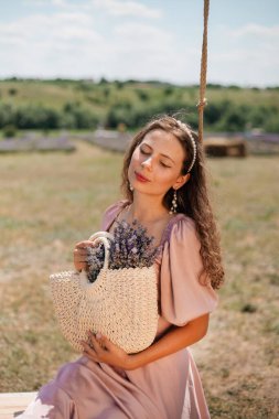 Genç bir kadın güneşli bir günde elinde çiçeklerle salıncakta sallanıyor.