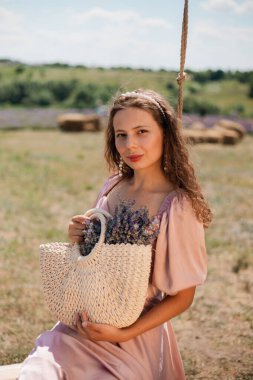 Genç bir kadın güneşli bir günde elinde çiçeklerle salıncakta sallanıyor.