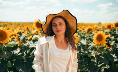 Ayçiçeği tarlasında güneşli bir öğleden sonra mavi gökyüzünün altında büyük bir şapka takan bir kadın.