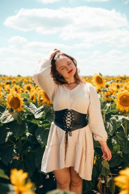 Kırsal kesimde yaz mevsimi boyunca, güneşli bir günde bir kadın gözlerinin önünde gülümserken, tarlada ayçiçekleri açar.