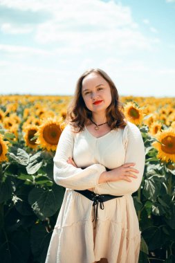 Kırsal kesimde yaz mevsimi boyunca, güneşli bir günde bir kadın gözlerinin önünde gülümserken, tarlada ayçiçekleri açar.