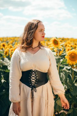 Kırsal kesimde yaz mevsimi boyunca, güneşli bir günde bir kadın gözlerinin önünde gülümserken, tarlada ayçiçekleri açar.