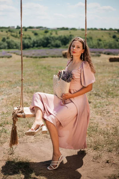 Genç bir kadın güneşli bir günde elinde çiçeklerle salıncakta sallanıyor.