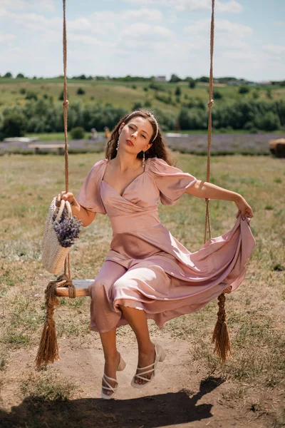 Genç bir kadın güneşli bir günde elinde çiçeklerle salıncakta sallanıyor.