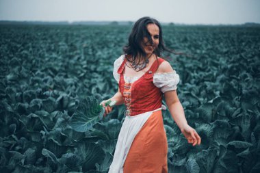 Kırsal kesimde bulutlu bir günde geleneksel giysiler içinde lahana tutan bir kadın.