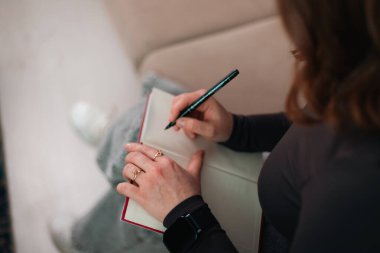 Turuncu aksanlı yastıklı rahat bir odada oturum sırasında psikolog notlar yazıyor.