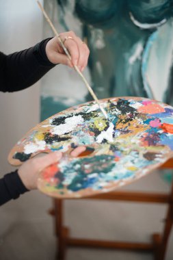 Sanatçı, gündüz saatlerinde stüdyoda renkli bir sanat eseri yaratırken bir palet dolusu boya tutuyor.