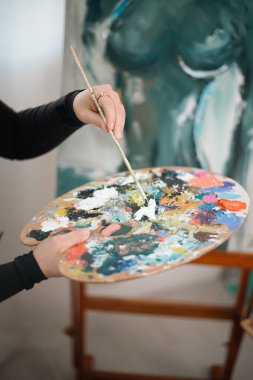 Sanatçı, gündüz saatlerinde stüdyoda renkli bir sanat eseri yaratırken bir palet dolusu boya tutuyor.
