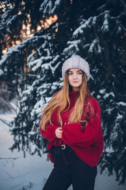 Genç bir kadın kış boyunca arka planda ağaçlarla karda durur.