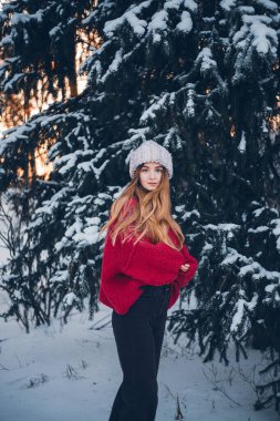 Genç bir kadın kış boyunca arka planda ağaçlarla karda durur.