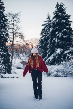 Kız kışın karlı arazide yürüyor Ağaçlar ve günbatımı arka planda parıldıyor