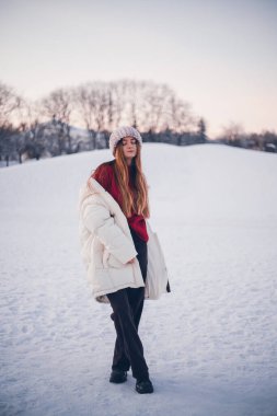 Kışın gün batımında, ağaçlar ve gökyüzü ile birlikte, kar üzerinde kalın bir palto giyen insan.