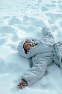 Kışın soğuk bir günde büyük bir kışlık palto giyerken karın içinde yatan kız.