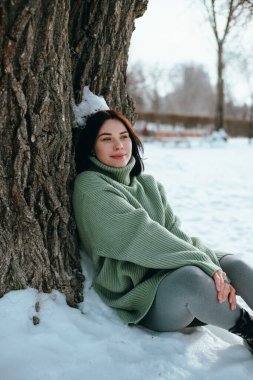 Kadın kış sahnesinde ağaç gövdesine oturmuş, karlı.