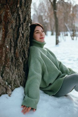 Kadın kış sahnesinde ağaç gövdesine oturmuş, karlı.