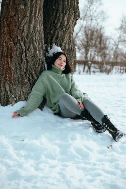 Kadın kış sahnesinde ağaç gövdesine oturmuş, karlı.