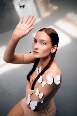 Model, gündüz saatlerinde stüdyoda el kaldırırken teninde kelebekler ile poz verir.