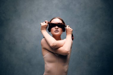 Model bir stüdyoda saç örgülü bir kıyafet giyip yaratıcı bir sanat ortamında kendine güven ve güç gösterisi yapıyor.