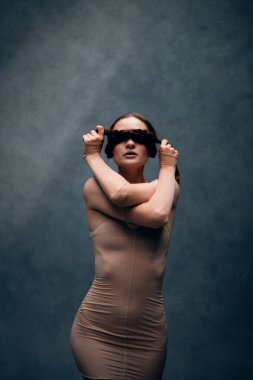 Model bir stüdyoda saç örgülü bir kıyafet giyip yaratıcı bir sanat ortamında kendine güven ve güç gösterisi yapıyor.