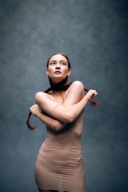 Model bir stüdyoda saç örgülü bir kıyafet giyip yaratıcı bir sanat ortamında kendine güven ve güç gösterisi yapıyor.