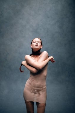 Model bir stüdyoda saç örgülü bir kıyafet giyip yaratıcı bir sanat ortamında kendine güven ve güç gösterisi yapıyor.