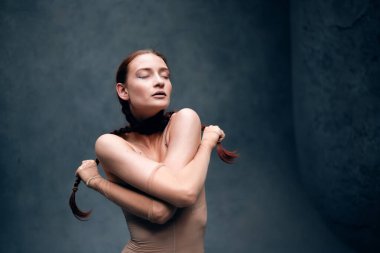 Model bir stüdyoda saç örgülü bir kıyafet giyip yaratıcı bir sanat ortamında kendine güven ve güç gösterisi yapıyor.