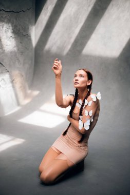 Model, gündüz saatlerinde stüdyoda el kaldırırken teninde kelebekler ile poz verir.