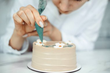 Şekerci, gün ışığında mutfak ortamında kremayla pasta süslüyor.
