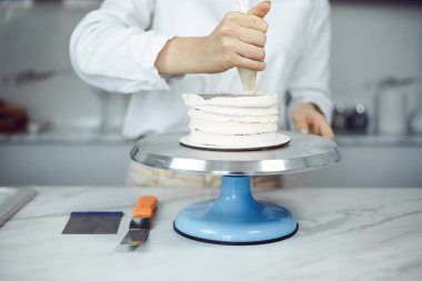 Şekerci, gündüz saatlerinde bir mutfakta pasta tezgahının üzerinde kremalı pasta hazırlar.