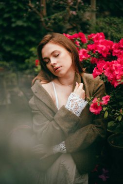 Güneşli bir öğleden sonra bahçedeki açelyaların yanında duran kadın.