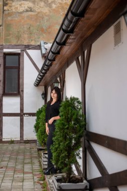 Güzel dikey portre. Şehvetli bir kadının görüntüsü, yüksek ve renkli, siyah elbiseli, duvarın yanında poz veren.